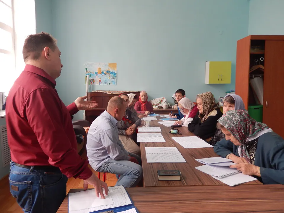 Взрослые за столом читают книгу под руководством преподавателя