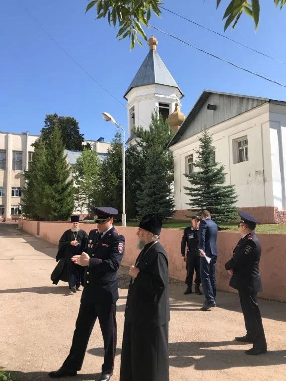 Архиерей и сотрудники полиции у входа в белый храм с куполом